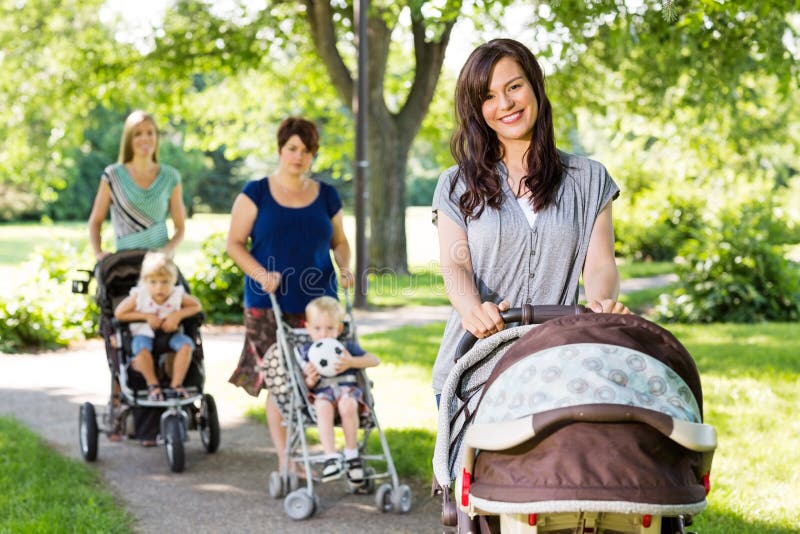 Schöne Mutter, die Kinderwagen im Park drückt lizenzfreie stockbilder