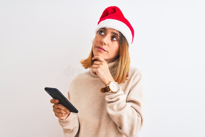 Schöne Rotkopffrau, die Weihnachtsmütze trägt und Smartphone seriöse Gesichter denken über Frage sehr verwirrte Idee stockfoto