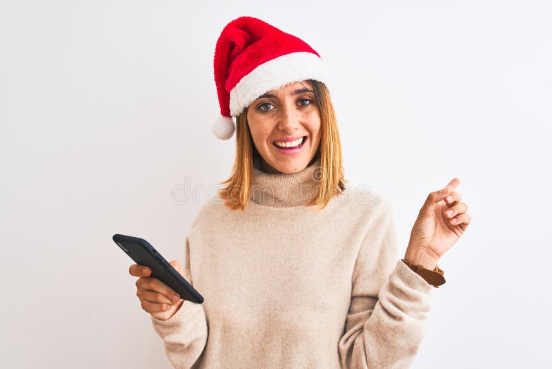 Schöne Rotkopffrau mit Weihnachtsmütze und Smartphone sehr glücklich mit Hand und Finger auf die Seite zeigen stockfotos