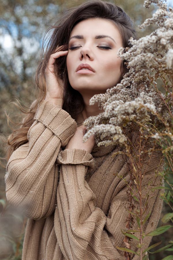 Schöne traurige nette attraktive Frau in einer beige Strickjacke weit auf einem Gebiet des trockenen Grases am kalten bewölkten T lizenzfreie stockfotos