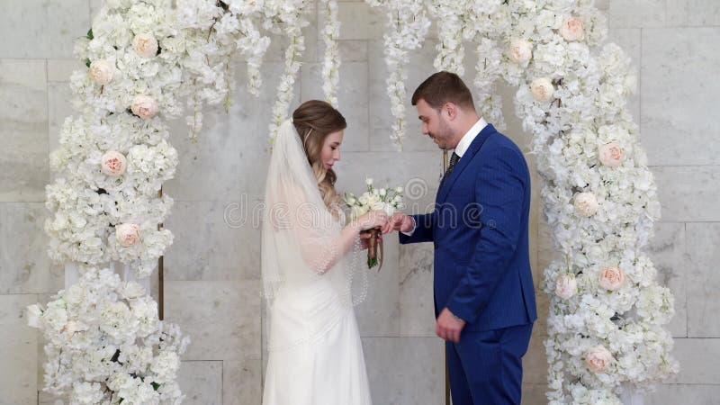 Schöne und glückliche Braut und Bräutigam Austausch Ringe in einem Bogen von Blumen