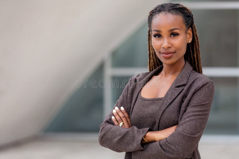 Schöne weibliche afrikanisch-amerikanische Geschäftsfrau CEO in einem Anzug am Arbeitsplatz, vertrauensvoll mit gefalteten Armen
