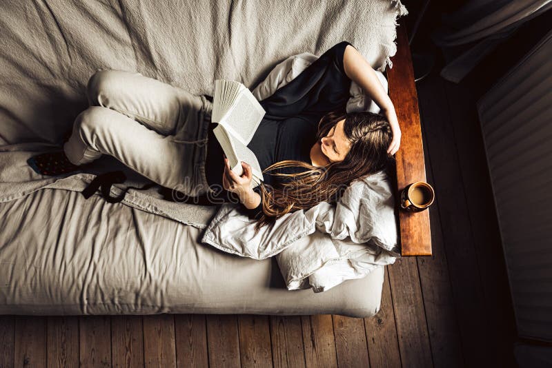 Schöner Blick auf eine 30 Jo Frau in ihrem Sofa, die ein Buch mit Kaffee liest