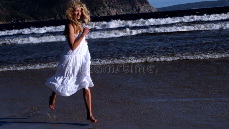 Schöner blonder Betrieb im weißen Kleid am sonnigen Tag am Strand