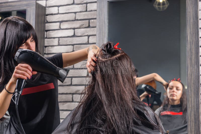 Schöner Friseur mit den tätowierten Händen unter Verwendung eines Haartrockners an lizenzfreie stockbilder Schöner Friseur mit den tätowierten Händen unter Verwendung eines Haartrockners an lizenzfreie stockbilder