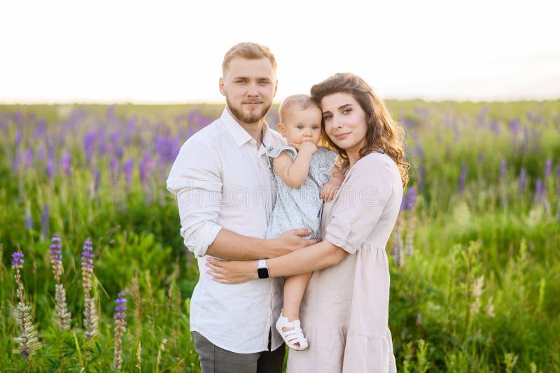 Schöner junger Familienvater und Mutter mit einem kleinen Mädchen, das auf einem Picknick sitzt lizenzfreies stockbild