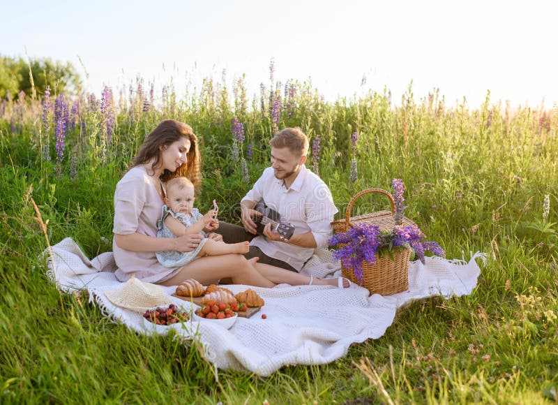 Schöner junger Familienvater und Mutter mit einem kleinen Mädchen, das auf einem Picknick sitzt lizenzfreies stockbild