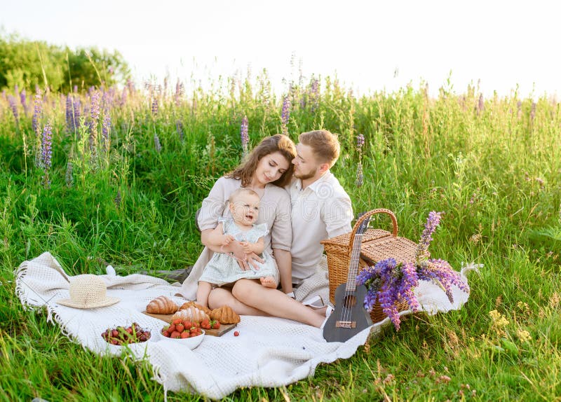 Schöner junger Familienvater und Mutter mit einem kleinen Mädchen, das auf einem Picknick sitzt stockfotos