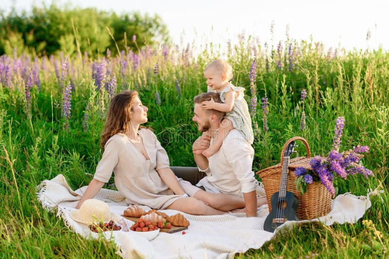 Schöner junger Familienvater und Mutter mit einem kleinen Mädchen, das auf einem Picknick sitzt lizenzfreies stockfoto