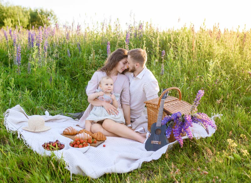 Schöner junger Familienvater und Mutter mit einem kleinen Mädchen, das auf einem Picknick sitzt stockfoto