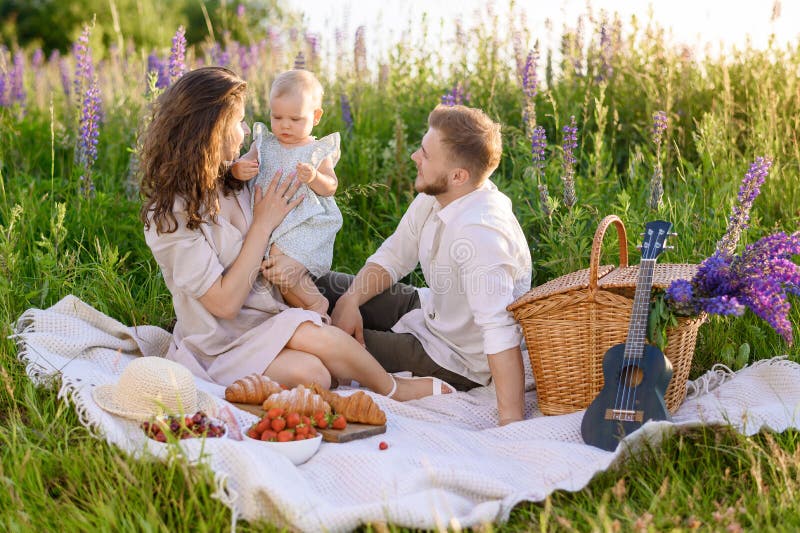 Schöner junger Familienvater und Mutter mit einem kleinen Mädchen, das auf einem Picknick sitzt stockfoto