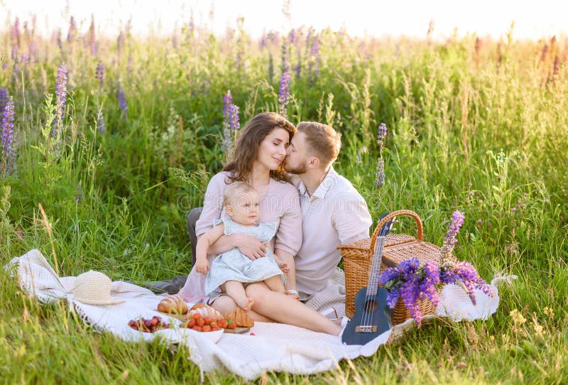 Schöner junger Familienvater und Mutter mit einem kleinen Mädchen, das auf einem Picknick sitzt stockfoto