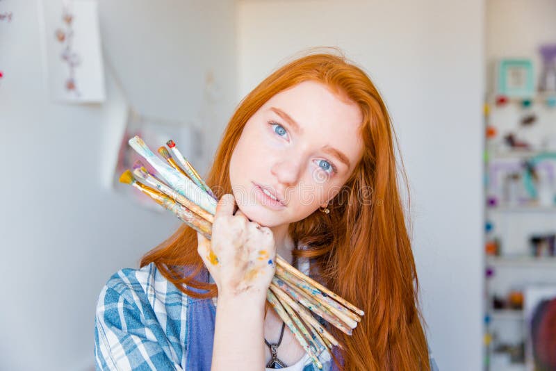 Schöner nachdenklicher Maler der jungen Frau, der Malerpinsel im Kunststudio hält stockfotografie Schöner nachdenklicher Maler der jungen Frau, der Malerpinsel im Kunststudio hält stockfotografie