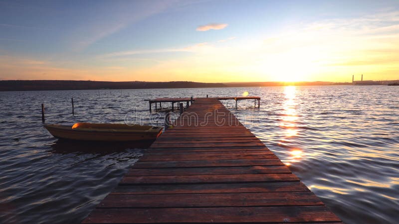 Schöner Sonnenaufgang. Boot und Holz Anlegestelle auf See mit einer Reflexion im Wasser bei Sonnenuntergang