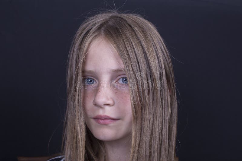 Beautiful blond young girl with freckles indoors on a black background, close up portrait. Beautiful blond young girl with freckles indoors on a black background, close up portrait