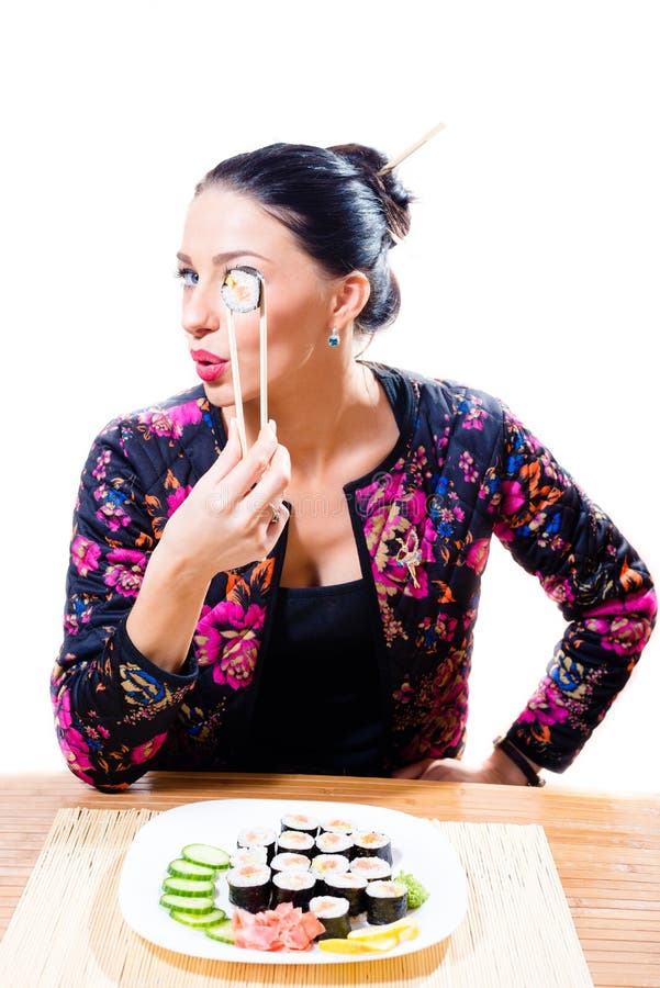 Schönes Brunettemädchen mit rote Lippenlustigen haltenen Essstäbchen und den schmecken Sushi, die Kamera auf weißem Hintergrundpo lizenzfreies stockfoto Schönes Brunettemädchen mit rote Lippenlustigen haltenen Essstäbchen und den schmecken Sushi, die Kamera auf weißem Hintergrundpo lizenzfreies stockfoto
