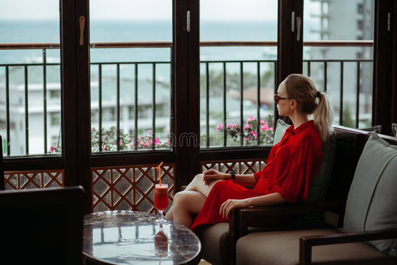 Schönes junges blondes Mädchen im roten Kleid und in der Sonnenbrille rotes Cocktail von einem Glas auf einer Freiterrasse von tr stockbild Schönes junges blondes Mädchen im roten Kleid und in der Sonnenbrille rotes Cocktail von einem Glas auf einer Freiterrasse von tr stockbild