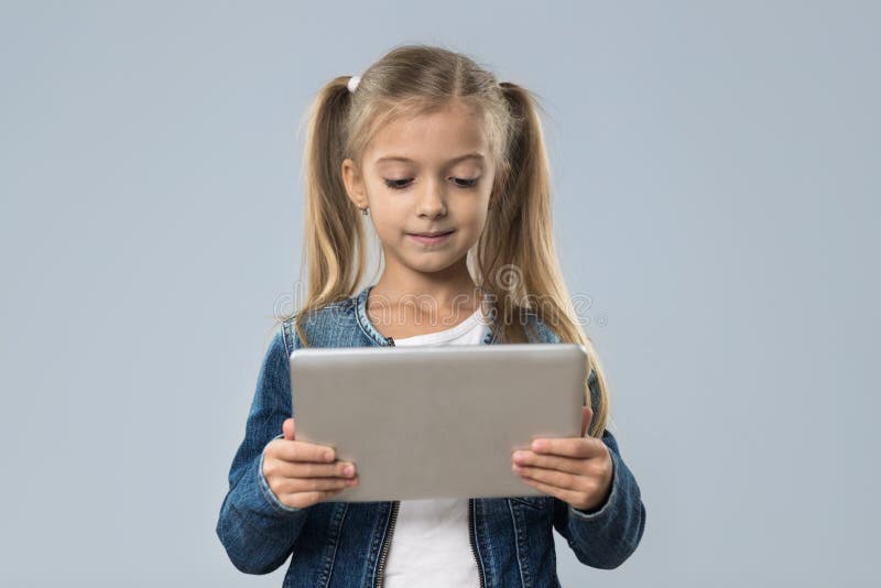 Schönes kleines Mädchen, das Tablet-Computer-den glücklichen lächelnden Abnutzungs-Jeans-Mantel lokalisiert verwendet stockbilder Schönes kleines Mädchen, das Tablet-Computer-den glücklichen lächelnden Abnutzungs-Jeans-Mantel lokalisiert verwendet stockbilder