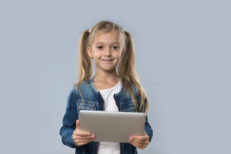 Schönes kleines Mädchen, das Tablet-Computer-den glücklichen lächelnden Abnutzungs-Jeans-Mantel lokalisiert verwendet stockfotografie Schönes kleines Mädchen, das Tablet-Computer-den glücklichen lächelnden Abnutzungs-Jeans-Mantel lokalisiert verwendet stockfotografie