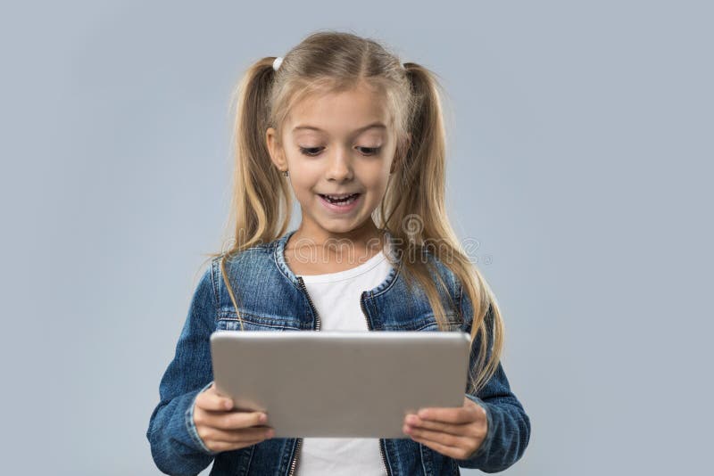 Schönes kleines Mädchen, das Tablet-Computer-den glücklichen lächelnden Abnutzungs-Jeans-Mantel lokalisiert verwendet lizenzfreie stockfotos Schönes kleines Mädchen, das Tablet-Computer-den glücklichen lächelnden Abnutzungs-Jeans-Mantel lokalisiert verwendet lizenzfreie stockfotos