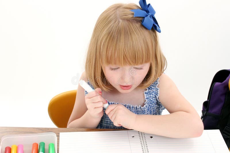 Schönes kleines Mädchen am Schreibtisch mit Kasten der Markierungen und des Notizbuches