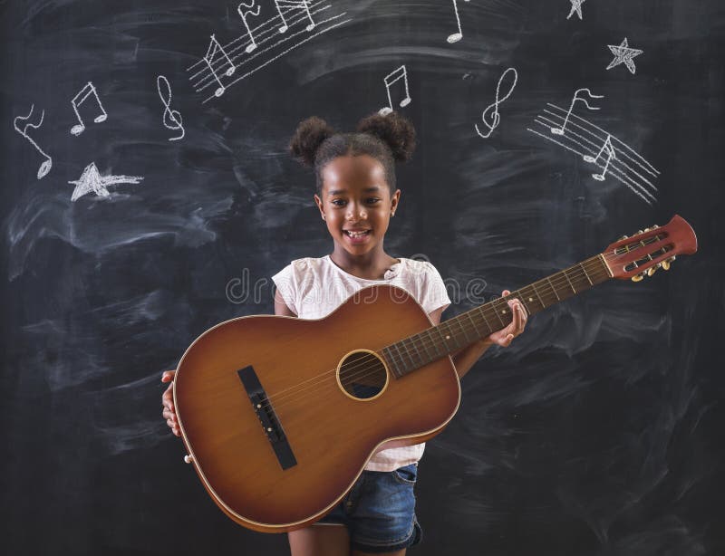 Schönes Mischrasseschulmädchen, welches die Gitarre während der Musikklasse spielt in der Schule lizenzfreies stockbild