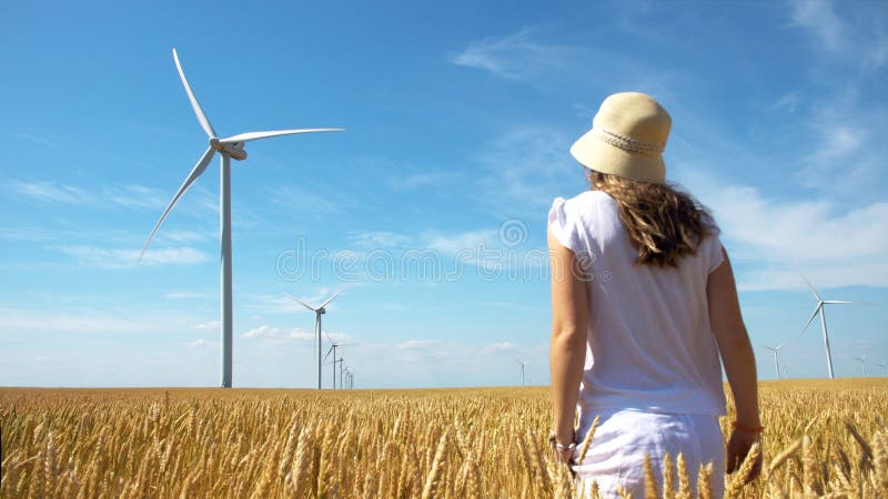 Schönes Mädchen auf gelbem Feld des Weizens mit Windmühlen für Produktion des elektrischen Stroms lizenzfreies stockfoto Schönes Mädchen auf gelbem Feld des Weizens mit Windmühlen für Produktion des elektrischen Stroms lizenzfreies stockfoto