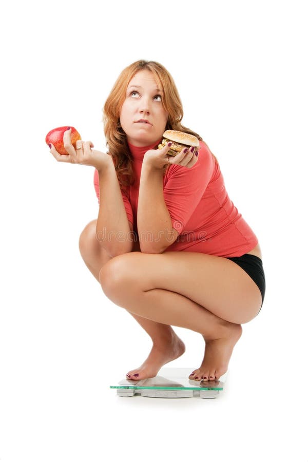 Beautiful girl sits on scales and chooses between an apple and a sandwich, isolated on white. Beautiful girl sits on scales and chooses between an apple and a sandwich, isolated on white