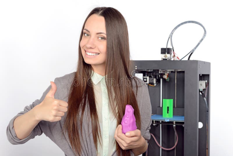 Beautiful young brunette student with long hair holding a violet item printed by a 3d-printer and smiling in a laboratory. Beautiful young brunette student with long hair holding a violet item printed by a 3d-printer and smiling in a laboratory