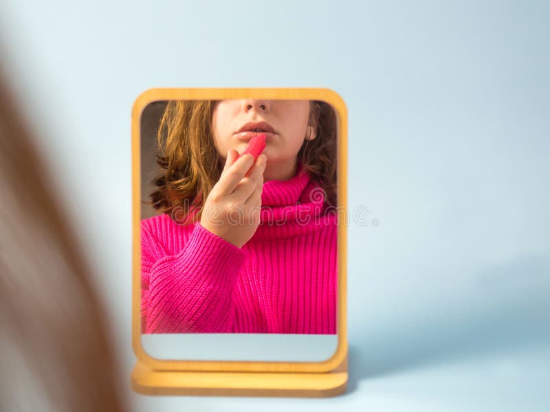 Schönes Mädchen schaut in den Spiegel und benutzt Lippenbalsam stockbilder