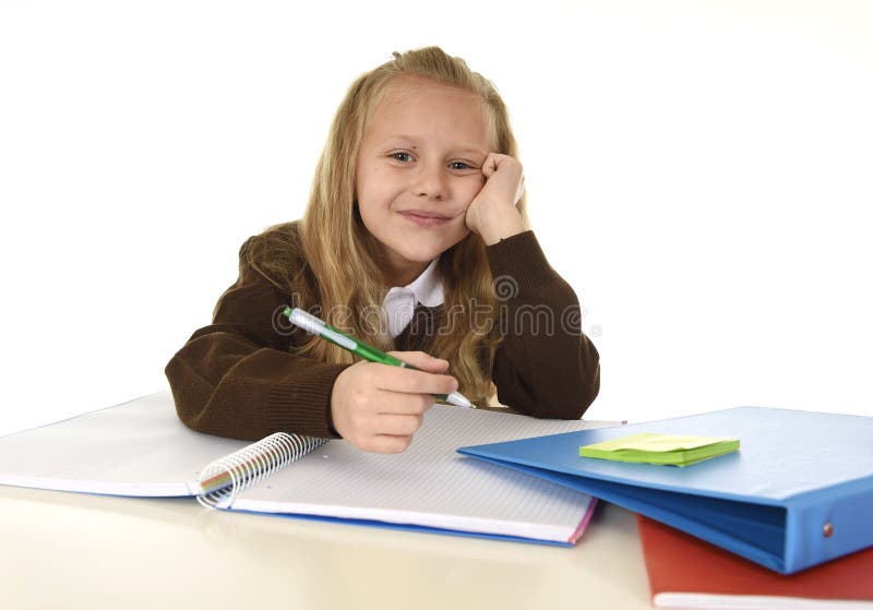 Schönes Schulmädchen in der Schuluniform mit lächelndem glücklichem Sitzen des blonden Haares auf dem Schreibtisch, der Hausarbei stockfoto Schönes Schulmädchen in der Schuluniform mit lächelndem glücklichem Sitzen des blonden Haares auf dem Schreibtisch, der Hausarbei stockfoto