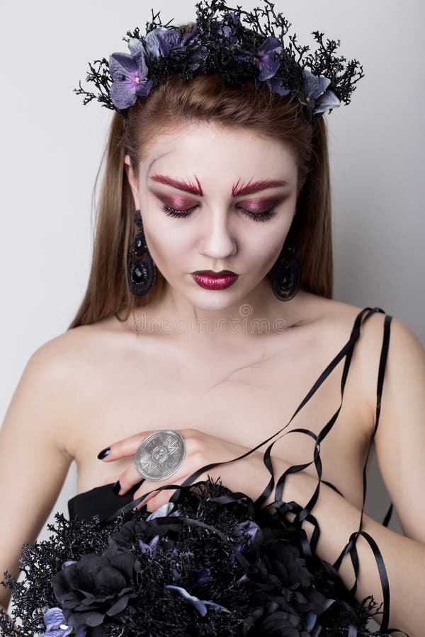 Schönes unverschämtes Mädchen im Bild eines Vampirs mit hellem dunklem Make-up, der schwarzen Vampirsbraut mit einem Blumenstrauß stockbilder