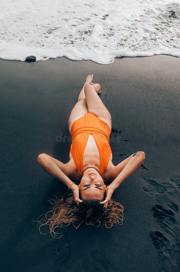 Schönheit liegt auf dem schwarzen Sandstrand in Bali, das orange Badeanzug trägt stockfotos Schönheit liegt auf dem schwarzen Sandstrand in Bali, das orange Badeanzug trägt stockfotos