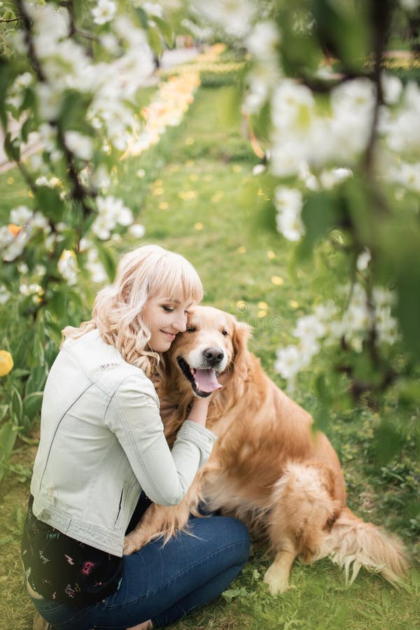 Schönheit mit einem netten golden retriever-Hund, der in den Blumen sitzt stockbild Schönheit mit einem netten golden retriever-Hund, der in den Blumen sitzt stockbild