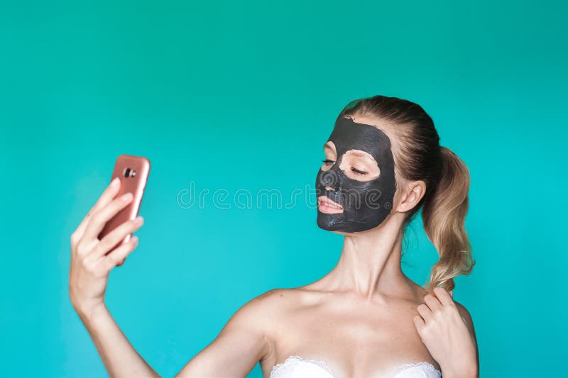 Schönheitsfoto einer Frau mit einer schwarzen Maske auf ihrem Gesicht hält ein Telefon in ihren Händen und macht selfie auf dem H lizenzfreies stockbild Schönheitsfoto einer Frau mit einer schwarzen Maske auf ihrem Gesicht hält ein Telefon in ihren Händen und macht selfie auf dem H lizenzfreies stockbild
