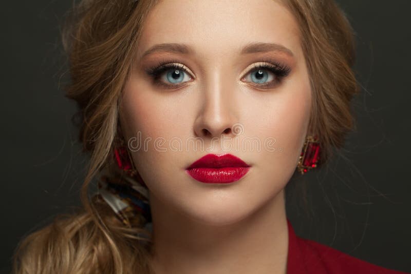 Beautiful woman face with blonde hair, red lips make up and red earrings on black. Beautiful woman face with blonde hair, red lips make up and red earrings on black.