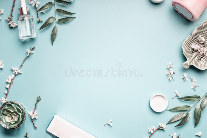 Schönheitshintergrund mit kosmetischen im Gesichtprodukten, Blättern und Kirschblüte auf blauem Tischplattenpastellhintergrund