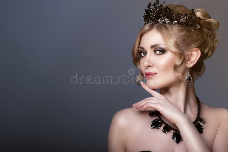 Schönheitsporträt des herrlichen jungen blonden Modells, das schwarze Juwelkrone und Satz luxuriöse Halskette und Ohrringe trägt lizenzfreie stockfotografie Schönheitsporträt des herrlichen jungen blonden Modells, das schwarze Juwelkrone und Satz luxuriöse Halskette und Ohrringe trägt lizenzfreie stockfotografie