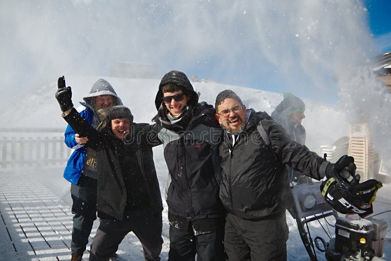 Les Orres, France - Circa 2015: Happy skiers posing for group photos while someone blasting snow on them using snow plowing machine to clear the terrace. People having fun. Les Orres, France - Circa 2015: Happy skiers posing for group photos while someone blasting snow on them using snow plowing machine to clear the terrace. People having fun