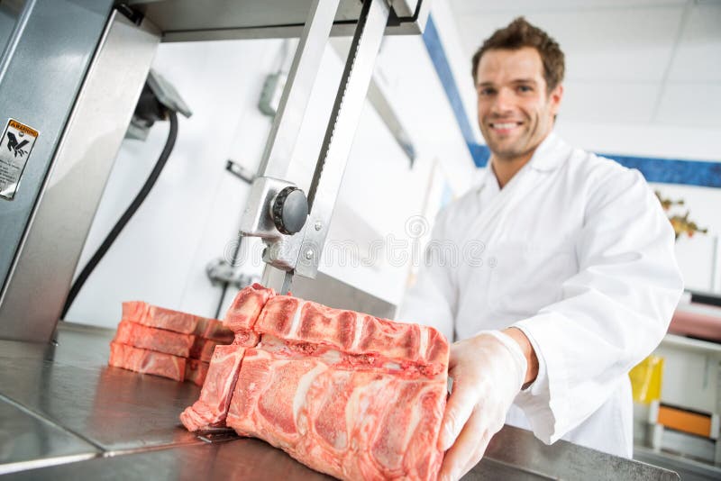 Scie à ruban masculine de Cutting Meat On de boucher images stock Scie à ruban masculine de Cutting Meat On de boucher images stock
