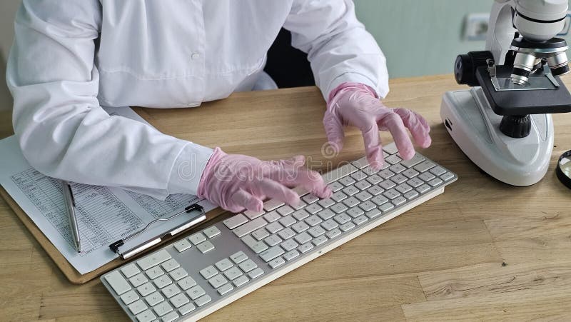 Scientist conducts research using keyboard and microscope in laboratory stock photography