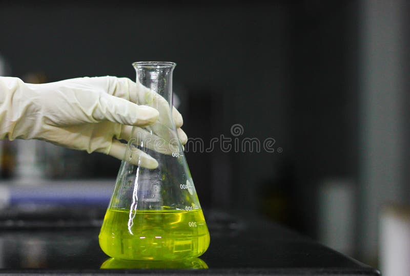 Scientist holding a glass conical flask in a gloved hand in chemistry laboratory
