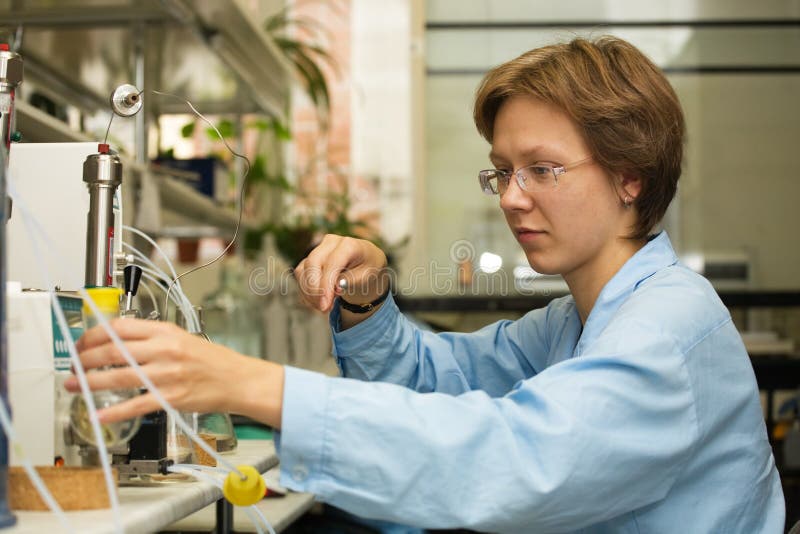 Il giovane bella donna-scienziato di lavoro con la siringa su uno sfondo di strumenti scientifici.