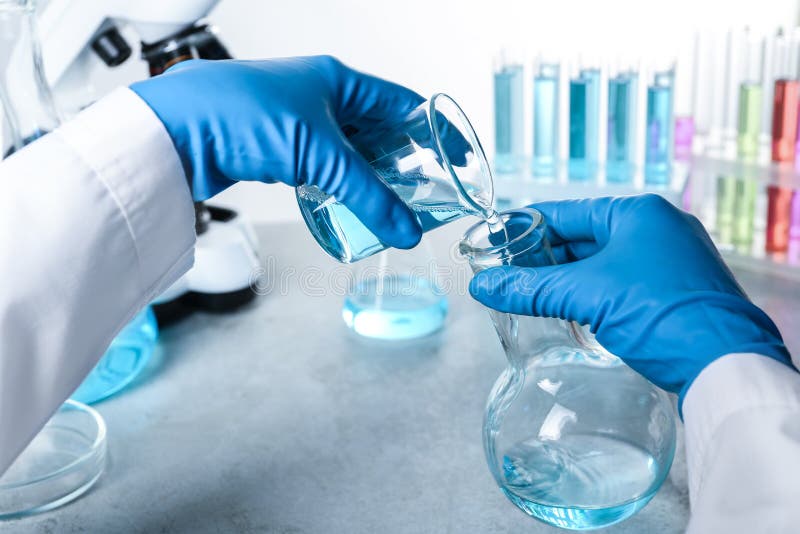 Scientist pouring color liquid from beaker into Florence flask over table, closeup stock photography