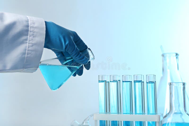 Scientist pouring color liquid from conical flask into test tubes on light background, closeup. Solution royalty free stock images