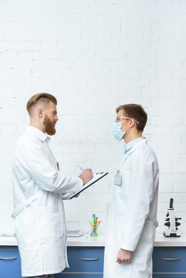 Scientists in White Coats Discussing Experiment Results in Lab Stock