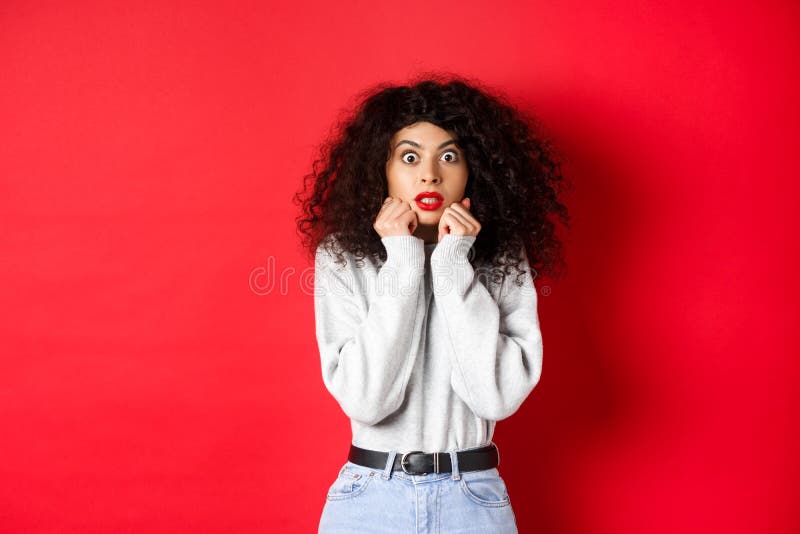 Scioccata donna caucasica con capelli ricci che guarda qualcosa di impressionante, raccapricciante e sorprendente mentre guarda l' fotografie stock