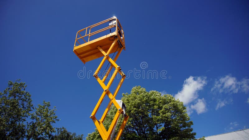 Scissor lift platform. With hydraulic system at maximum height range painted in orange colors, large construction machine, heavy industry, white clouds and blue royalty free stock photos Scissor lift platform. With hydraulic system at maximum height range painted in orange colors, large construction machine, heavy industry, white clouds and blue royalty free stock photos
