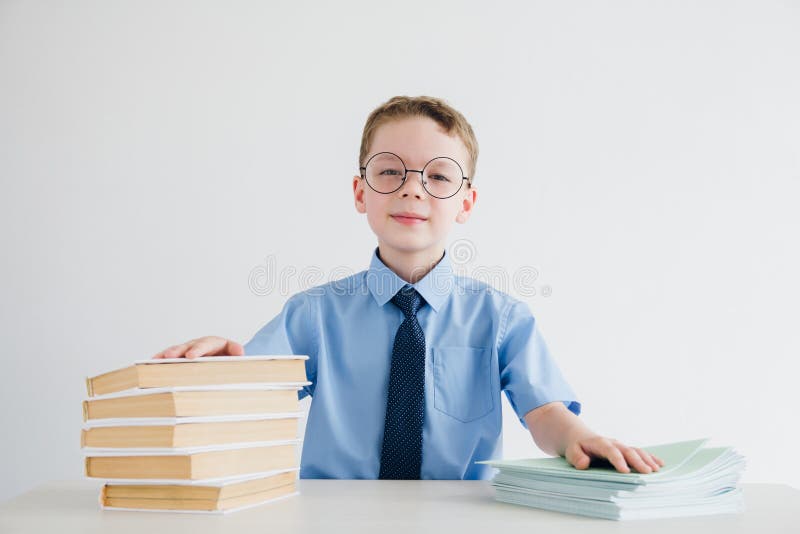 Scolaro in uniforme scolastico che si siede ad uno scrittorio con i manuali e fotografia stock libera da diritti Scolaro in uniforme scolastico che si siede ad uno scrittorio con i manuali e fotografia stock libera da diritti