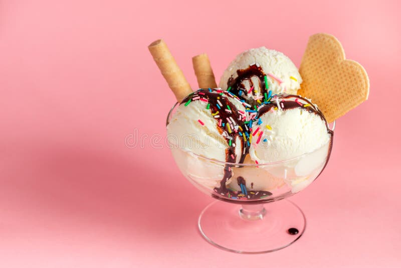 vanilla flavor ice cream in glass bowl with chocolate sauce, strewed sprinkles and waffle cookies on pink background